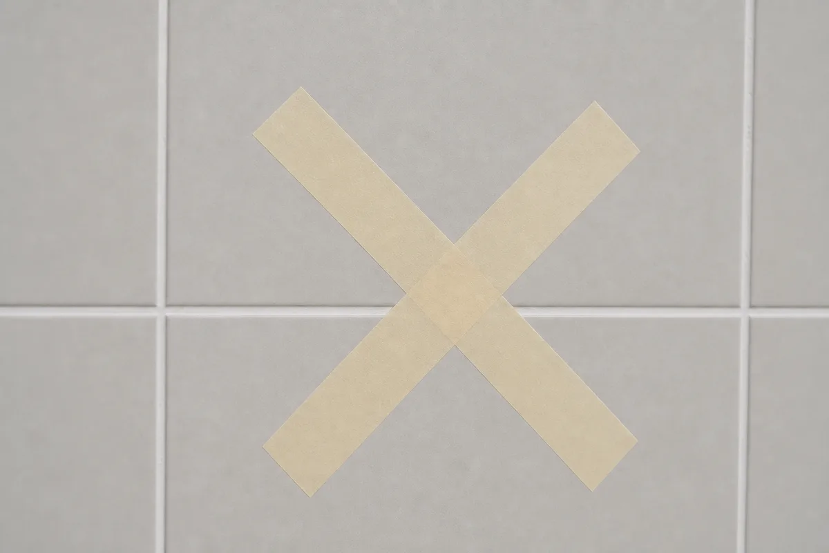 Croix de ruban de masquage collée sur un carreau de faïence gris clair avant perçage